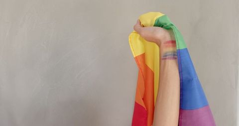 Arm holding draped rainbow flag with colorful arm painting