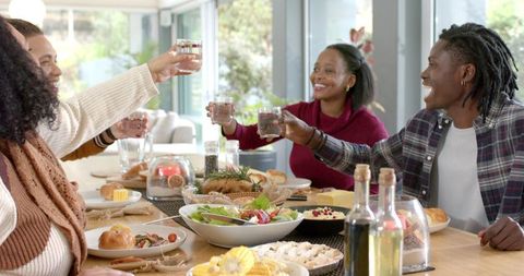 Diverse friends raising glasses around cozy family-style dinner table celebrating together
