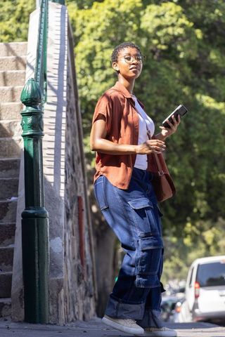 African american woman standing on city sidewalk holding smartphone and bag in sunlight