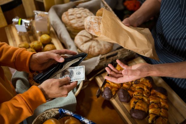 Customer paying with cash at a bakery counter, showing a variety of fresh bread and pastries. Ideal for use in articles or advertisements related to small businesses, retail transactions, bakery promotions, or cash payments.