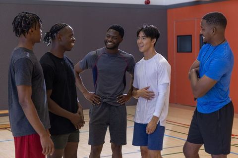 Multicultural male teammates chatting and laughing in indoor gym court wearing sportswear