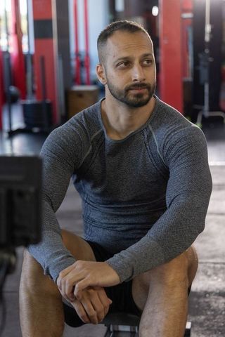 Indian fitness man resting between sets on bench in gym, contemplative and focused