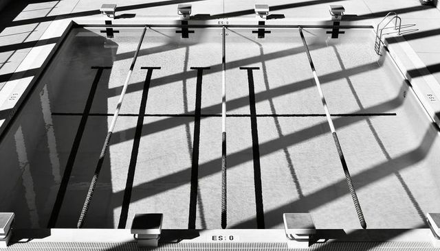 Empty Indoor Pool Revealing Lane Lines and Dramatic Window Shadows in High-Contrast Monochrome