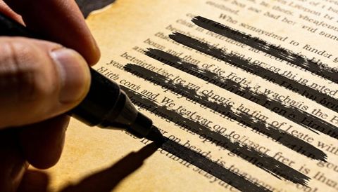 Adult Hand Redacting Text with Black Marker on Yellowed Paper Closeup Censorship Concept