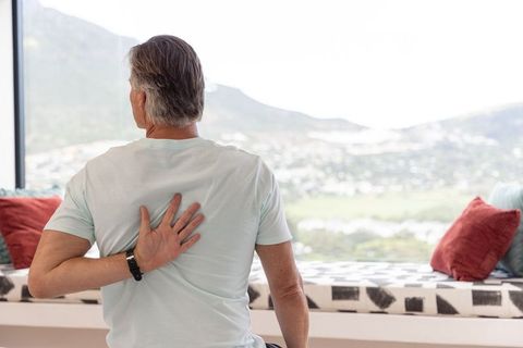 Mature man sitting on window seat reaching back for shoulder gazing at sunlit valley view