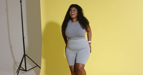 Curvy african american woman smiling in gray workout set on vibrant yellow studio backdrop