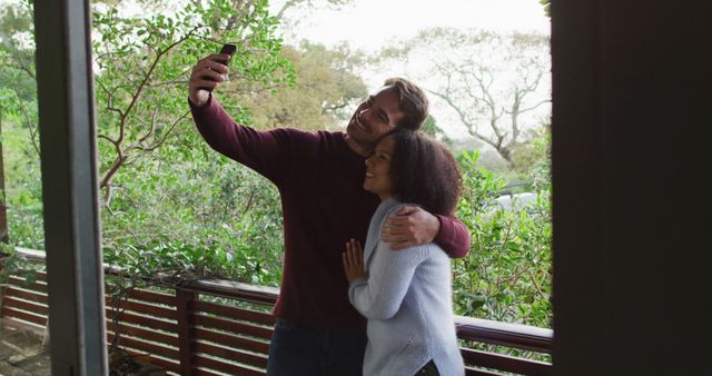 Happy diverse couple looking at smartphone and talking, standing on balcony in the countryside - Download Free Stock Photos Pikwizard.com