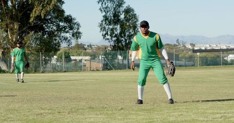 African American Baseball Outfielders in Green Yellow Uniforms Fielding on Sunny Grass Field