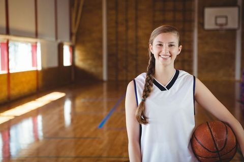 Teenage Girl Holding Basketball Smiling in School Gymnasium
