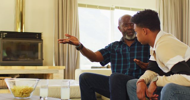 African american father and adult son talking and watching sport on tv - Download Free Stock Photos Pikwizard.com