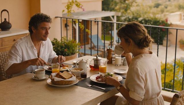 Couple enjoying linen breakfast on sunlit balcony with bread basket and coffee