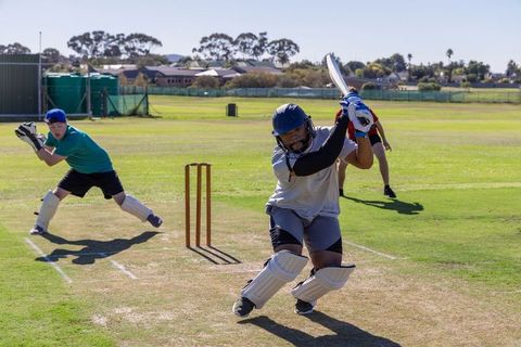 Batsman driving powerful shot on sunny cricket pitch with wicketkeeper and fielder