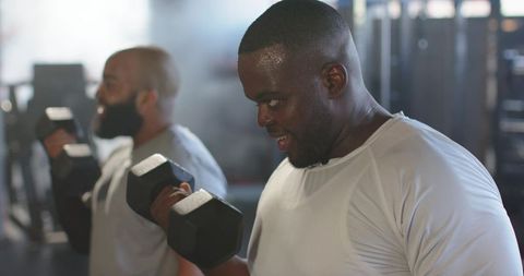 African american men lifting heavy dumbbells, sweating, focusing on strength training