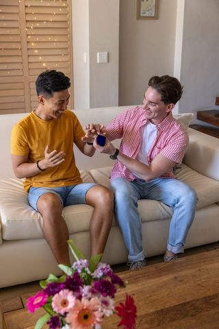 Surprise proposal at home: joyful same-sex couple celebrating engagement on sofa
