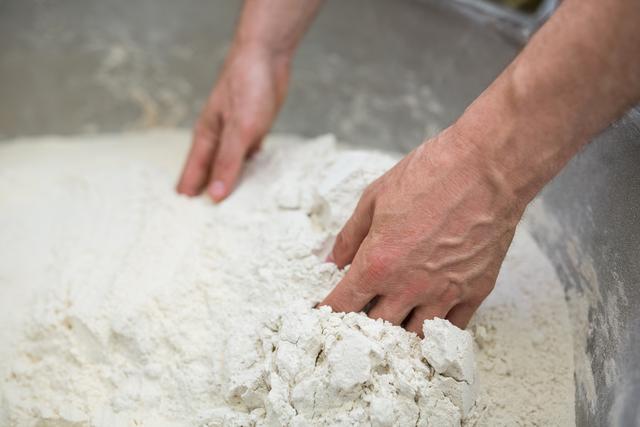 This close-up captures hands mixing flour, ideal for illustrating processes related to baking and homemade cooking. Perfect for food blogs, recipe websites, cooking tutorials, and culinary magazines.