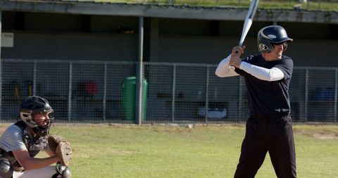 Batter preparing to swing while catcher crouching at sunny community baseball field