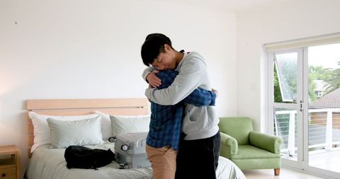 Father and son embracing in bedroom with suitcase packing