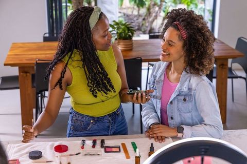 Diverse women filming beauty tutorial with smartphone and ring light at home