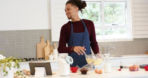 Smiling African American man stirring batter in modern kitchen following tablet recipe