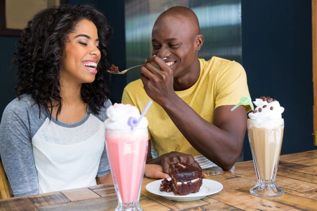Loving young man feeding dessert to woman in coffee shop