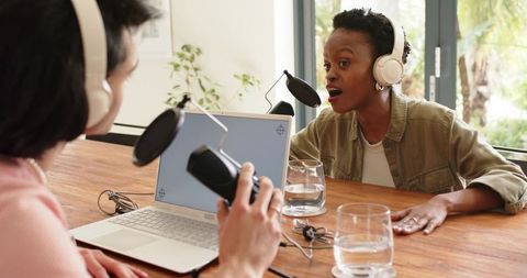 Diverse co-hosts recording lively podcast at studio table with laptop and microphones