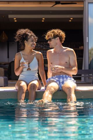 Couple relaxing by pool dipping feet and sipping drinks on sunny modern terrace
