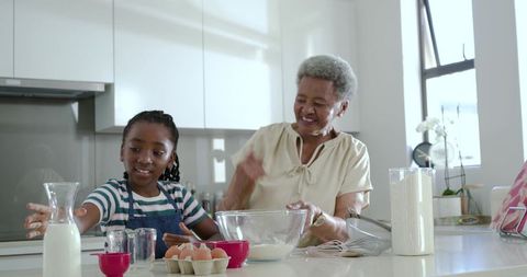 African grandmother and granddaughter baking together in bright modern kitchen teaching family recip
