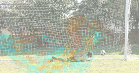Goalkeeper diving to save soccer ball with turquoise and orange particle burst in goal