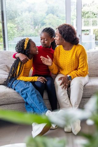 African american mother sharing conversation and hugs with daughters on living room sofa