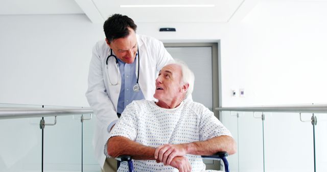 This image depicts a doctor assisting a senior man in a wheelchair, presumably in a hospital corridor. The doctor is wearing a lab coat and has a stethoscope, symbolizing professionalism and medical care. This image is useful for illustrating medical assistance, healthcare services, and patient-doctor relationships in a hospital environment.