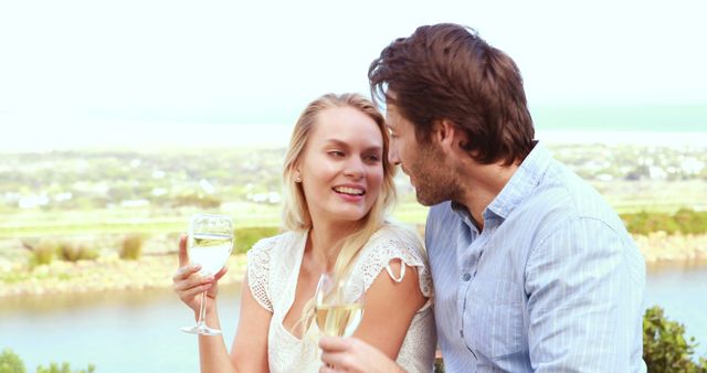 A young Caucasian couple enjoys a romantic moment with glasses of wine, with copy space. They are sharing a toast, celebrating a special occasion, against a scenic backdrop.
