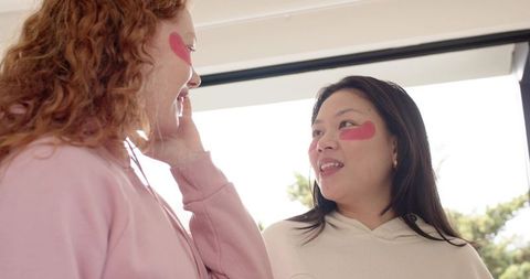 Two friends wearing hydrogel under-eye patches sharing skincare moment in sunlit room