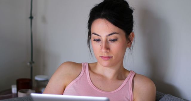 Young woman using a tablet at home, focused and engaged. Ideal for depicting technology use, education, remote work, leisure activities, or home lifestyle. Perfect for blogs about tech gadgets, working from home, or modern living.