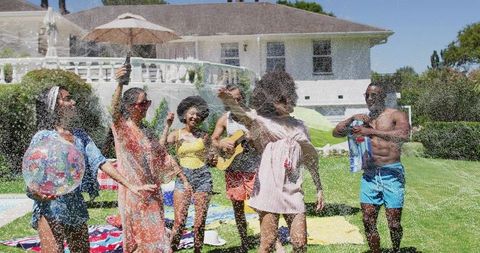 Friends dancing at backyard pool party spraying bottle and playing guitar