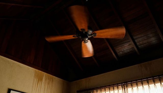 Spinning wooden ceiling fan creating motion blur in rustic vaulted room with damp streaks
