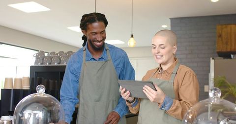 Diverse baristas reviewing tablet orders behind cafe counter with pastry domes