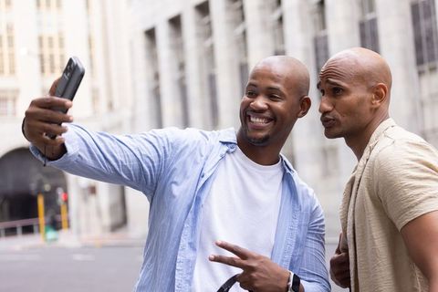 Friends taking selfie on city street smiling and posing, casual urban men capturing joy