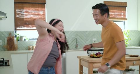 Playful couple laughing and dancing in bright modern kitchen with island
