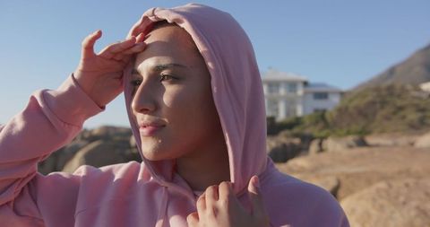 Contemplative woman in pink hoodie enjoying coastal view