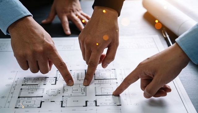 Three hands pointing at residential floor plan examining design details collaboration
