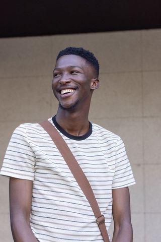 Smiling young african man wearing striped tee and crossbody bag against beige wall