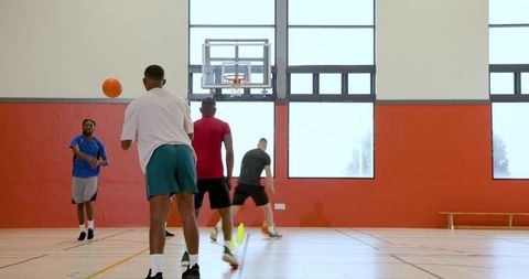 Five men practicing basketball passing drill on indoor court with cones and hoop