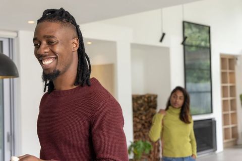 Smiling man holding white coffee mug while partner watches in modern minimalist living room