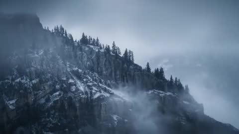 Drone sweeping through drifting fog revealing rugged alpine ridge with pines and snow