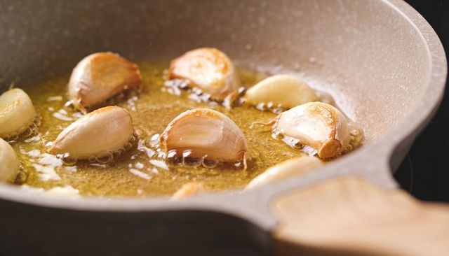 Sizzling garlic cloves browning in golden oil in nonstick pan with wooden handle closeup