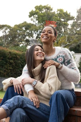 Smiling diverse friends embracing outdoors wearing merry christmas headbands and knit sweaters