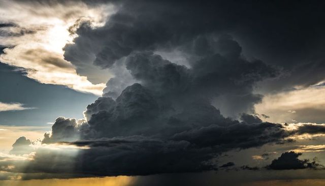 Rising cumulonimbus towering over plains casting crepuscular rays and rain shaft