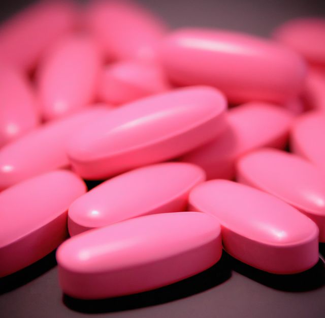 Close up of multiple pink pills laying on black background. Medicine, healthcare and treatment concept.