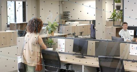 Bringing plant to desk: woman placing greenery in modern open-plan office while colleague gesturing