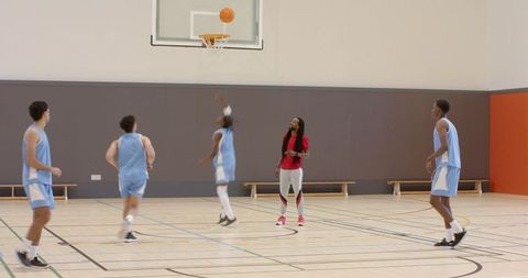 Basketball team training on indoor court with coach guiding players